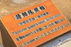 女王の頭の周囲に集まる観光客と4か国語の注意書き