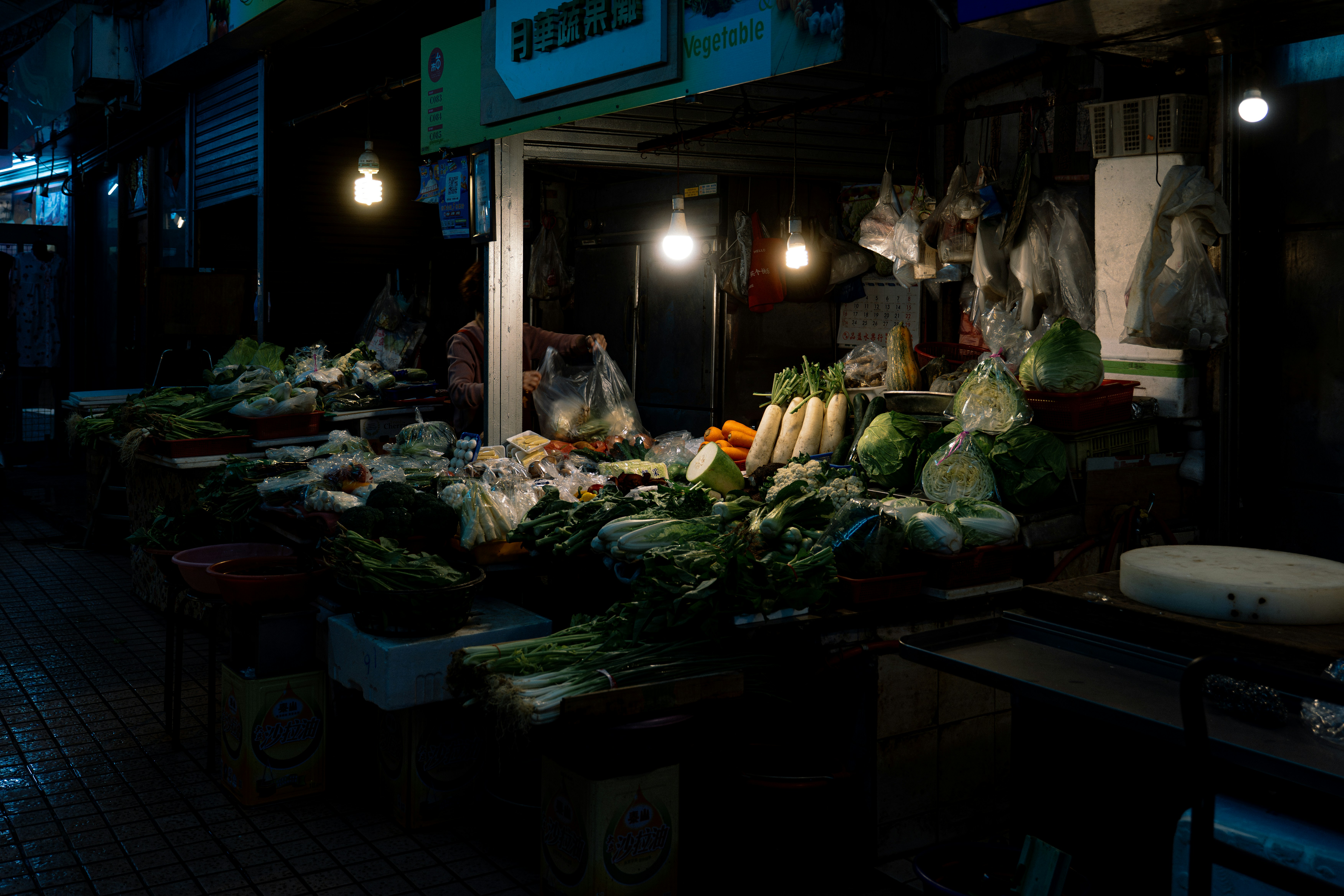 A dimly lit market stall displaying fresh vegetables at night.