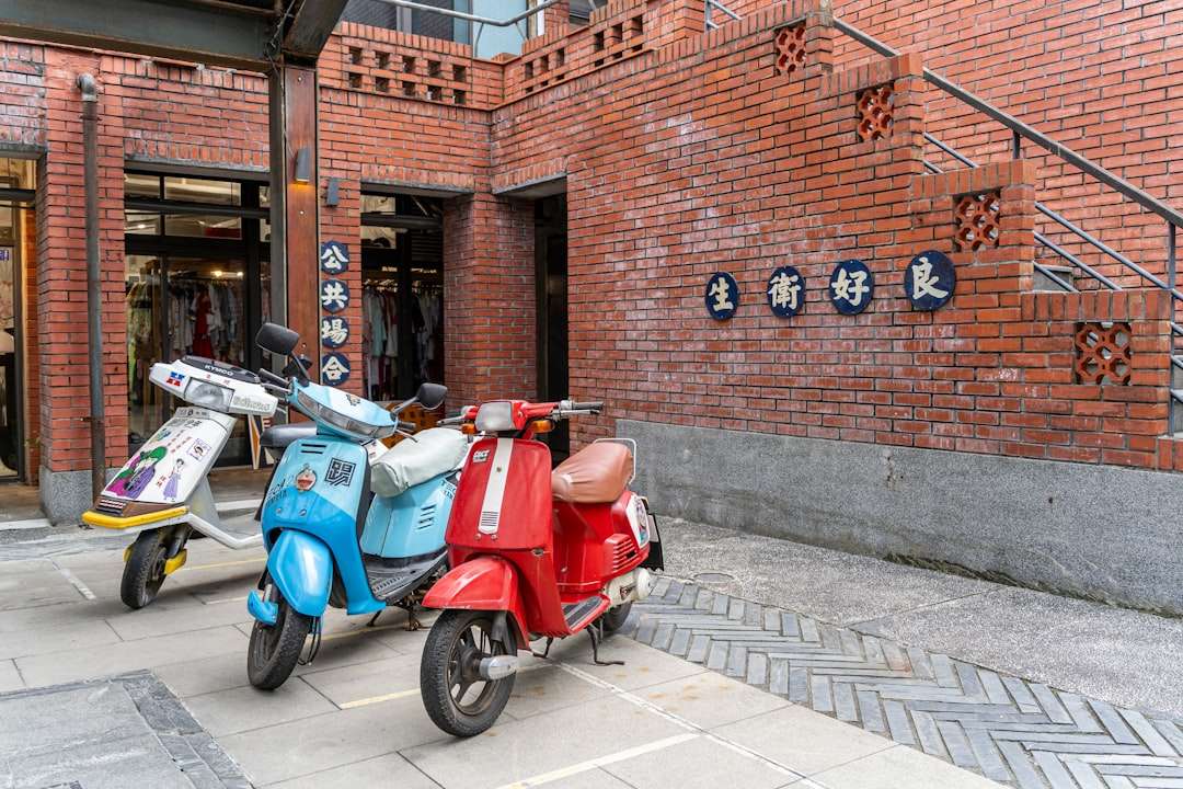 Three colorful scooters parked outside a brick building.