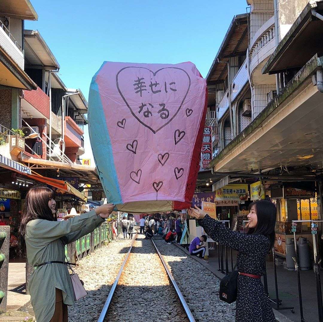 十分老街の線路脇で天燈を空に放つ旅行者たち。ランタンがゆっくりと夜空に昇っていく