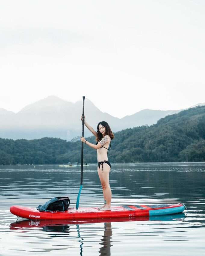 旅行者が日月潭の湖面でSUPに立って漕いでいる。背景に緑の山並みが広がる