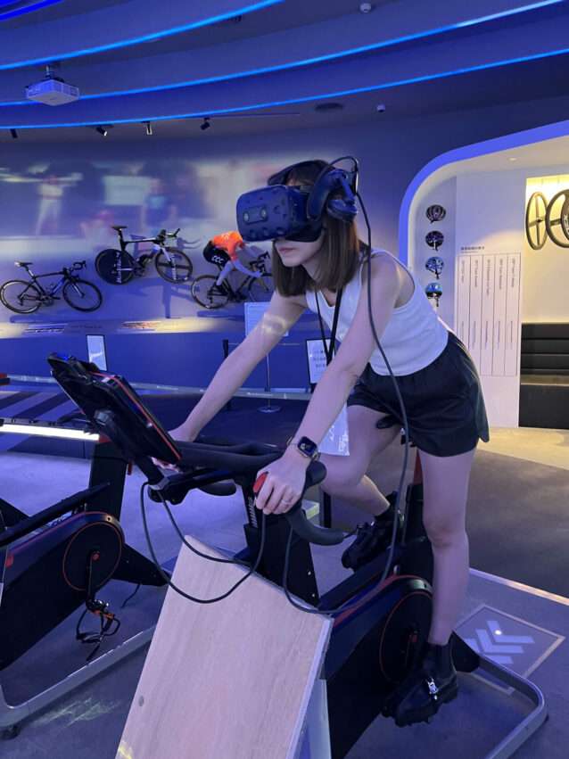 自転車文化探索館のVR乗車体験エリア。ヘルメットをつけた来館者が仮想空間でのサイクリングを体験している