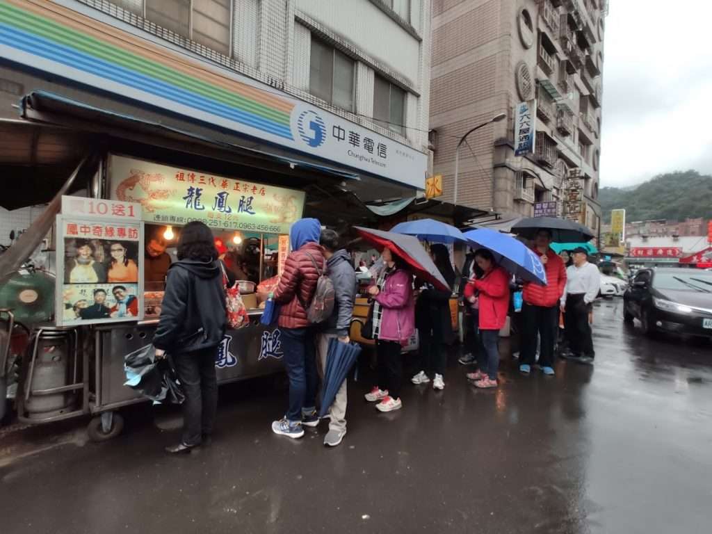 瑞芳老街の屋台前に並ぶ旅行者たち。看板には「阿霞龍鳳腿」の文字
