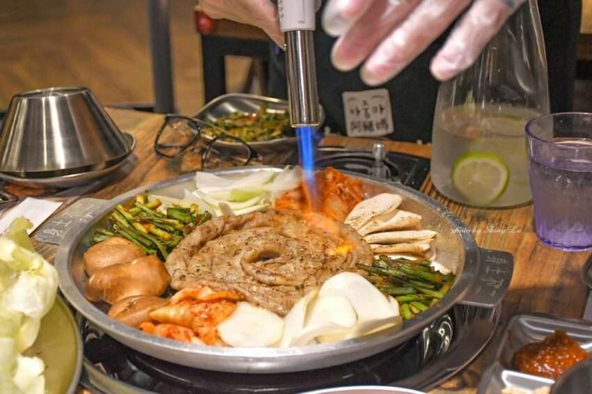 阿豬媽韓式烤肉吃到飽の焼肉台。複数の肉と韓国おかずが並んでいる