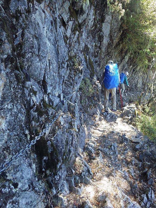 岩壁に沿った狭い山道を進む登山者