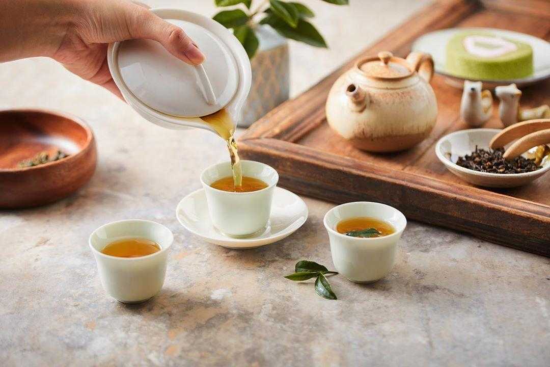 白磁の急須から小さな杯へ注がれる金黄色の茶湯。卓上には茶葉と茶壺が並ぶ