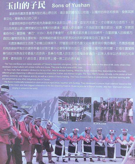 玉山の子民と題された看板の前に立つ原住民の伝統衣装を着た人々